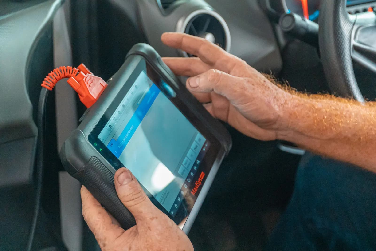 Diagnostiikkalaite kytkettynä autoon, asentaja käyttää laitteen kosketusnäyttöä